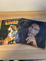 Two vinyl record albums 'Live!' and 'Legend' by Bob Marley and The Wailers shown side by side on a wooden surface.