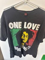 Front view of black Bob Marley T-shirt featuring colorful print with 'ONE LOVE' text, face of Bob Marley in yellow, green, red, and text 'BOB MARLEY'