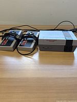 Photo showing the NES console with two wired controllers and cables, laid on a wooden surface.