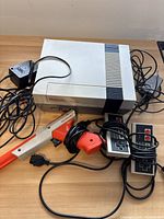 Photo showing NES console with power supply, two wired controllers, and Zapper light gun on the table.