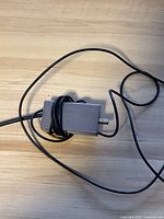 Gray rectangular Nintendo RF switch device with attached cable coiled on light wood surface