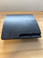 Front and top view of black PlayStation 3 console showing PS3 logo on top and power button on front.