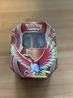 A closed metal collectible tin with Ho-Oh artwork on the lid and Pokémon Trading Card Game logo above a window.