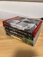 Stack of five PlayStation 3 game cases showing titles on spines: Tomb Raider, Call of Duty World at War, Call of Duty Black Ops, Medal of Honor, Resident Evil 5