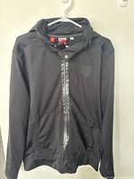 Front view of the black Puma full zip hoodie jacket with Scuderia Ferrari logo on the chest, showing hood and pockets.