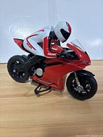 Side view of red Ducati RC motorcycle toy with rider figure dressed in white and red gear. Motorcycle shows realistic details like suspension and decals.