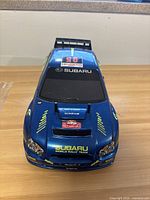 Front view of blue Subaru Impreza WRC RC car body with decals on a wooden surface.