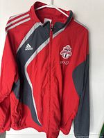 Full view of red Adidas Toronto FC training jacket with zip front, showing logo and color blocking.