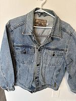 Front of vintage Armani Jeans denim jacket on hanger, showing light blue wash and button closure.