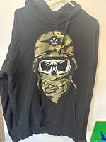 Front of black Rocca Wear hoodie with skull and camouflage helmet graphic.
