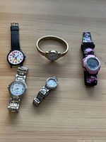 Top view showing all five wristwatches including cartoon, gold-tone, pink digital, large two-tone Timex, and small silver watch.