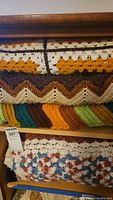 Stack of four crocheted afghans placed on shelves showing various color schemes and crochet patterns.