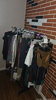 View of clothing rack loaded with assorted women's clothes including black pants, patterned dresses and blouses.