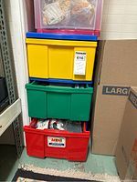 Three drawers stacked plastic storage bin in basement, showing red, green, yellow drawers with craft items inside.