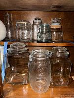 Overview of assorted clear glass jars on wooden shelves: including Mason jars with hinged lids, glass-lidded jars, and cork-topped jars.