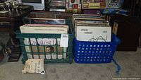 Two plastic crates filled with various LP vinyl records placed on a carpeted floor, showing album spines and covers in mixed condition.