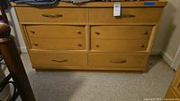 Front view of mid-century modern wooden dresser with brass-look hardware and six drawers, showing handles and knobs, with some minor surface scratches.
