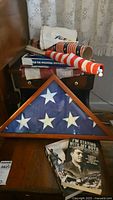 View showing folded triangular framed American flag, assorted rolled flags and cloths, and two displayed military history books.