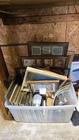 Tote bucket filled with multiple picture frames made of wood and some brass accents, stacked vertically showing variety in sizes and styles.
