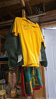 Yellow Eastern Star polo shirt with embroidery, hanging in front of a dark green jacket and a blanket.