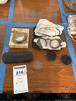 Antique eyeglasses, silver frames, brass swan magnifier, monocles, and eye accessories arranged on table.