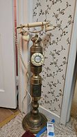 Full view of the vintage floor-standing ornate brass rotary phone showing entire height and base detail