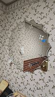 Mirror on floral wallpapered wall showing scalloped, star-like edge design with reflective surface showing ceiling light and surrounding room details.