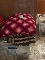 Pink and white crocheted afghan featuring circular flower-like motifs folded over a plastic bin.