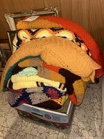 Stack of five folded afghans in different colors and patterns placed in a box.