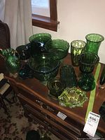 Full assortment of green vintage art glass items including vases, bowls, and compotes on wooden table