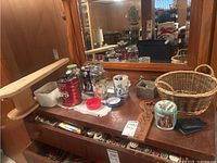 Photo shows multiple containers on a wooden surface including jars and tins filled with assorted buttons, a wire basket, and some wallets.