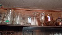 Wide view of glass vases including clear glass and carnival glass items on a shelf, showing various shapes and sizes including tall and shorter vases, some with textured or patterned glass.