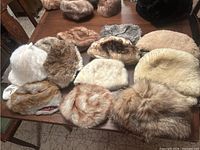 Wide shot of 11 fur hats of various colors and fur types on a wooden table.