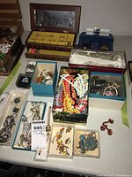Tabletop overview of assorted jewelry boxes and trays with rings, bead necklaces, earrings, bracelets and watch