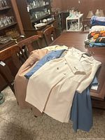 Seven vintage ladies long coats in cream, blue, tan colors stacked on a wooden table