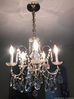 Chandelier hanging from ceiling, lit with six candle-style light bulbs, showing detail of crystals and arms.