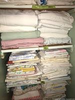 Two shelves filled with folded bed linens and pillowcases in various colors and patterns, showing overall lot contents.