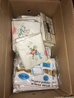 Box containing vintage pillowcases featuring colorful floral embroidery and packaged pillow protectors.