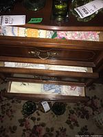 Wooden drawers open showing multiple folded table linens and napkins including floral fabric and crocheted pieces