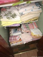 Two shelves packed with neatly folded bed linens, towels, tea towels and face cloths showing floral patterns and assorted pastel colors.