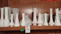 Shelf with multiple vintage milk glass vases in different shapes and textures, including hobnail and scalloped designs.