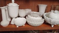 Group overview of assorted milk glass pieces on wooden shelf
