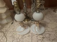Pair of vintage milk glass hobnail lamps on tiled floor, showing full lamps with cords wrapped around bases.