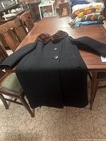 Black ribbed textured long ladies coat spread open on wooden table with brown mink collar, large buttons, and two pockets visible.