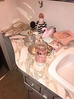 Dresser top showing assorted bathroom accessories, decorative figurines including a small doll, pink swan, and lidded jars.