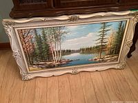 Front view of the oil painting in its decorative frame showing the full landscape scene of trees and a lake.