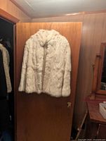 Rabbit fur coat hanging on a wooden door, showing front view and plush fur texture.