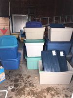 Photo showing stacked plastic storage bins of varied colors and sizes including blue, green, white, beige, and cream bins with matching lids in an open garage.