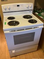 Frontal shot of white Amana electric stove showing all four coil burners and control panel.