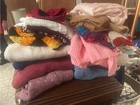 Stack of various hand knit woolen sweaters in colors like pink, blue, brown, yellow, white and red on a small table.